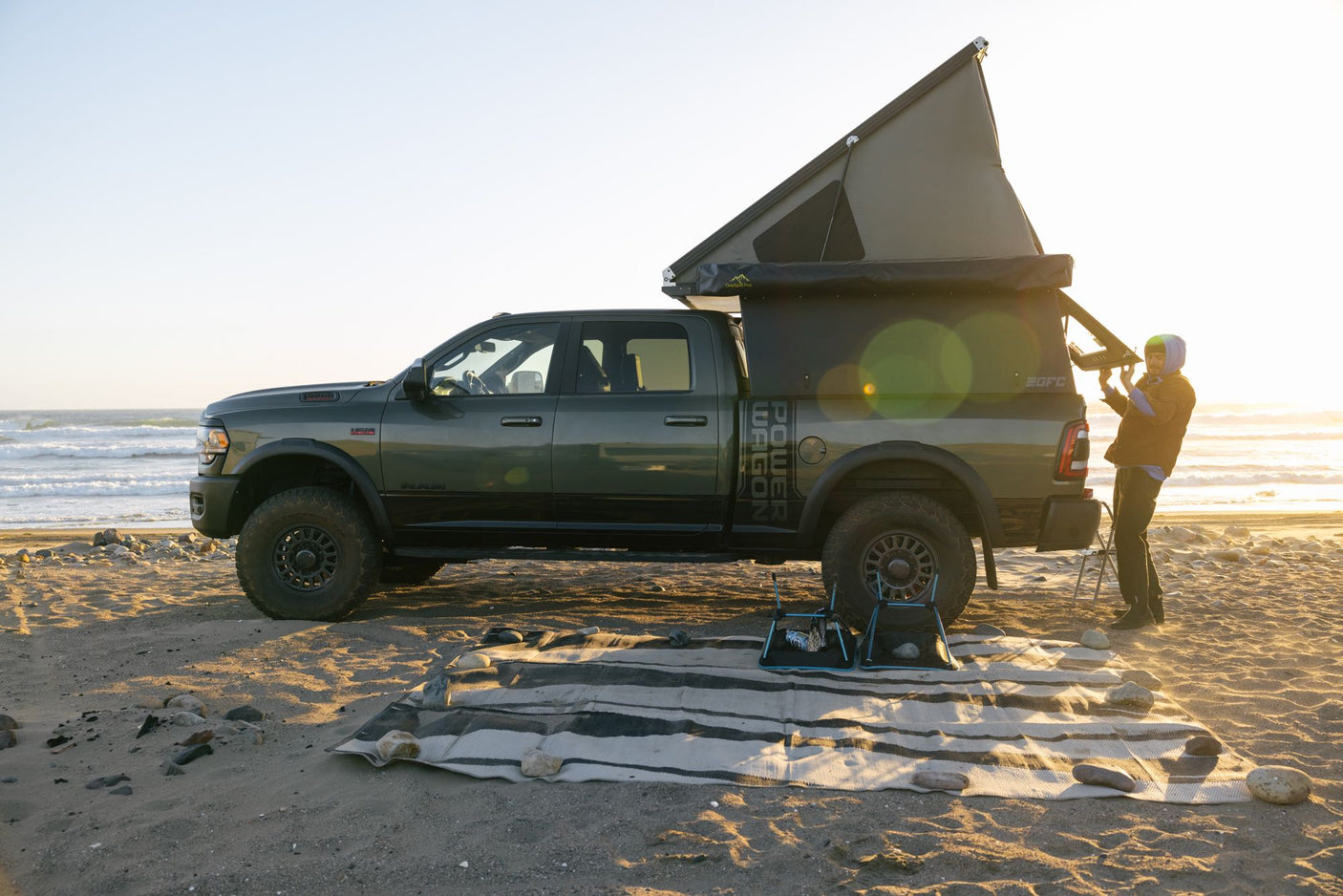 Ram Power Wagon with an overlanding camper on a beach at sunset. Ideal RV rental for ocean adventures.