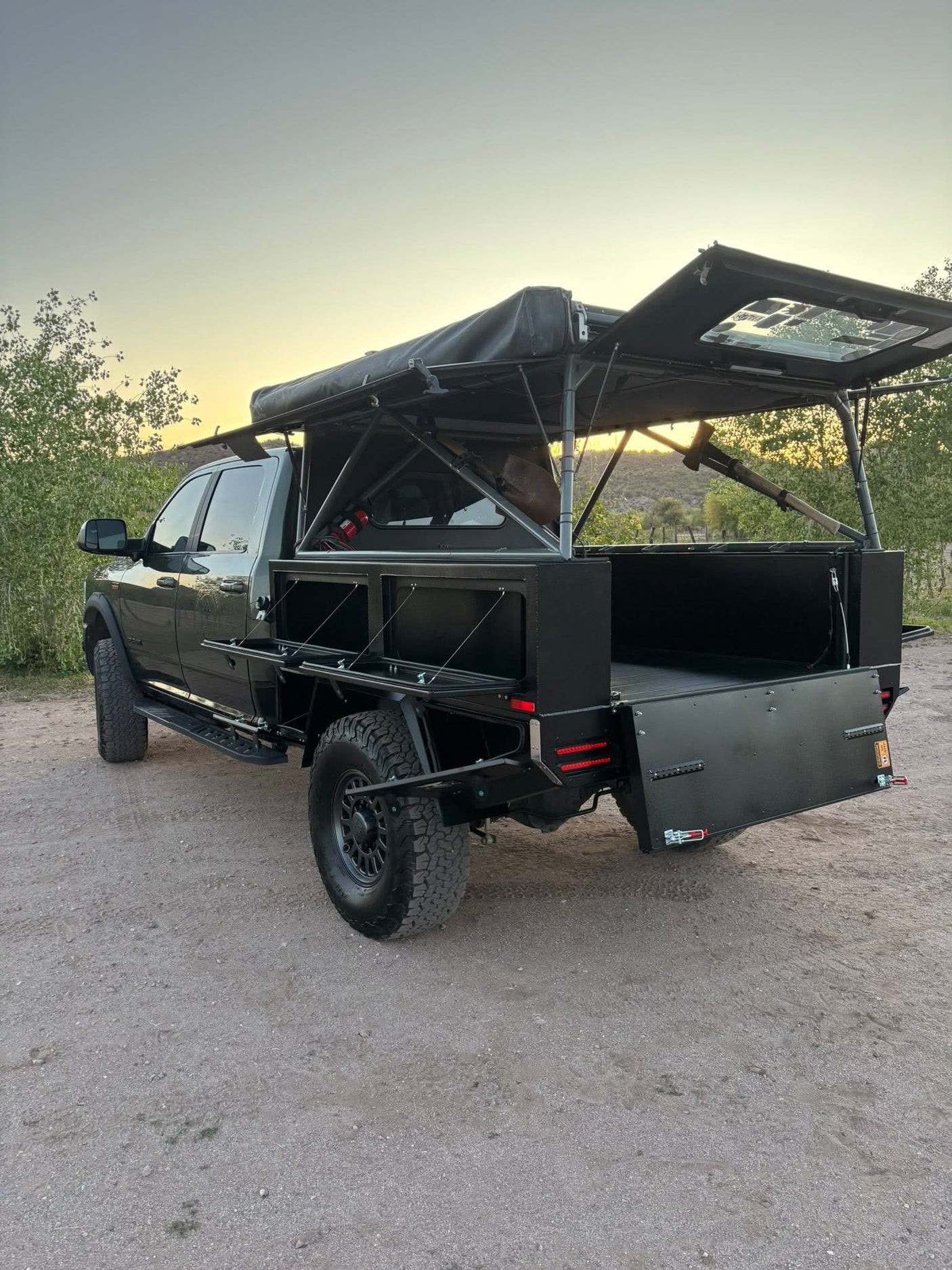 A custom dark gray overland truck with a flatbed conversion & open rooftop tent, ideal for rugged RV rental adventures.