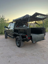 A custom dark gray overland truck with a flatbed conversion & open rooftop tent, ideal for rugged RV rental adventures.