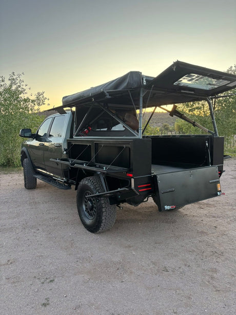 A custom dark gray overland truck with a flatbed conversion & open rooftop tent, ideal for rugged RV rental adventures.