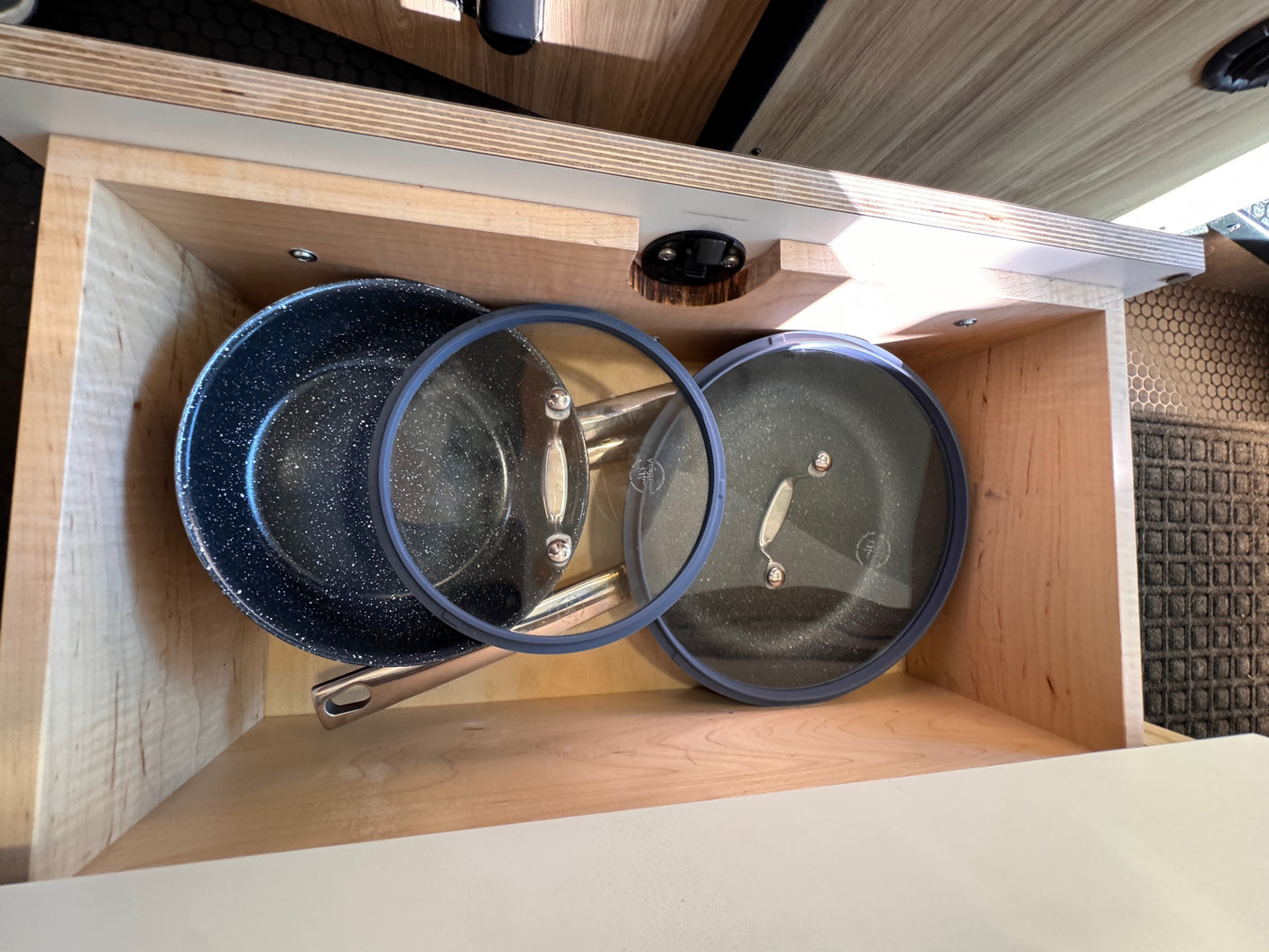 RV rental kitchen: Neatly stored pots & pans with glass lids in a compact wooden drawer, optimizing space for travel.