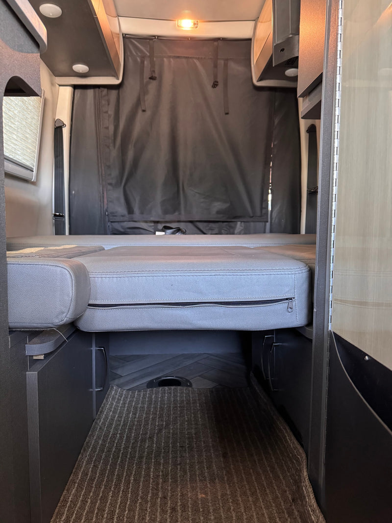 Experience comfort in this RV rental with its convertible bed, overhead storage, and rear privacy curtain. — photo 8