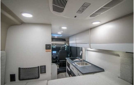 Modern rv rental interior with a compact kitchen, overhead storage, and a comfy bed, leading to the driver's cabin.