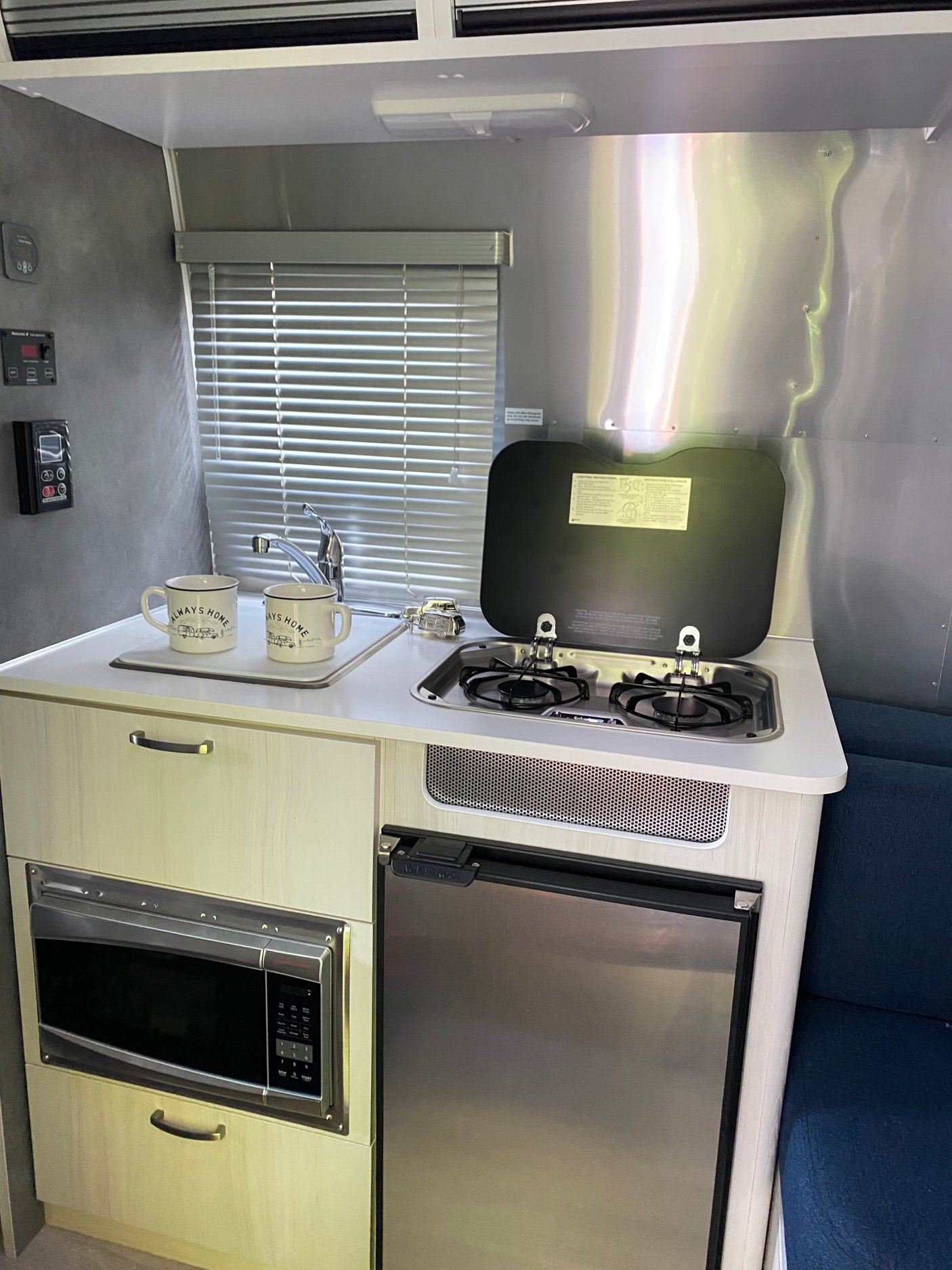 Compact RV rental kitchen features a sink, stove, microwave, and refrigerator, offering all essentials for travel convenience.