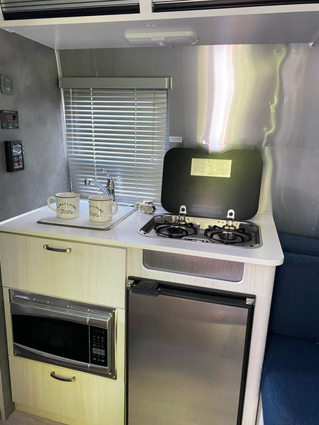 Compact RV rental kitchen features a sink, stove, microwave, and refrigerator, offering all essentials for travel convenience.