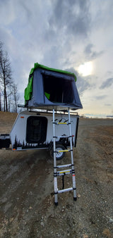 RV rental: A compact travel trailer with a deployed rooftop tent and ladder is ready for outdoor camping adventures.