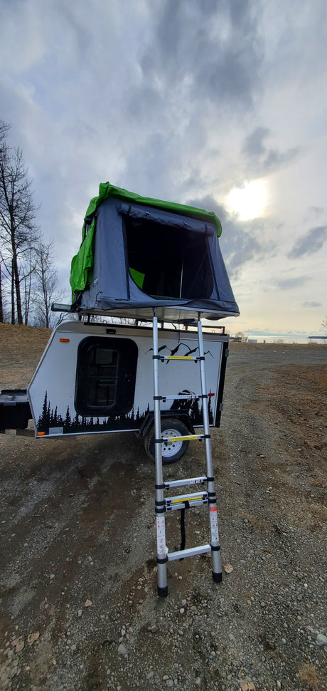 RV rental: A compact travel trailer with a deployed rooftop tent and ladder is ready for outdoor camping adventures.