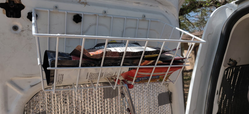 RV rental storage: A white wire basket holds food pouches, mounted on the inside of a van door for organized travel snacks. — photo 9