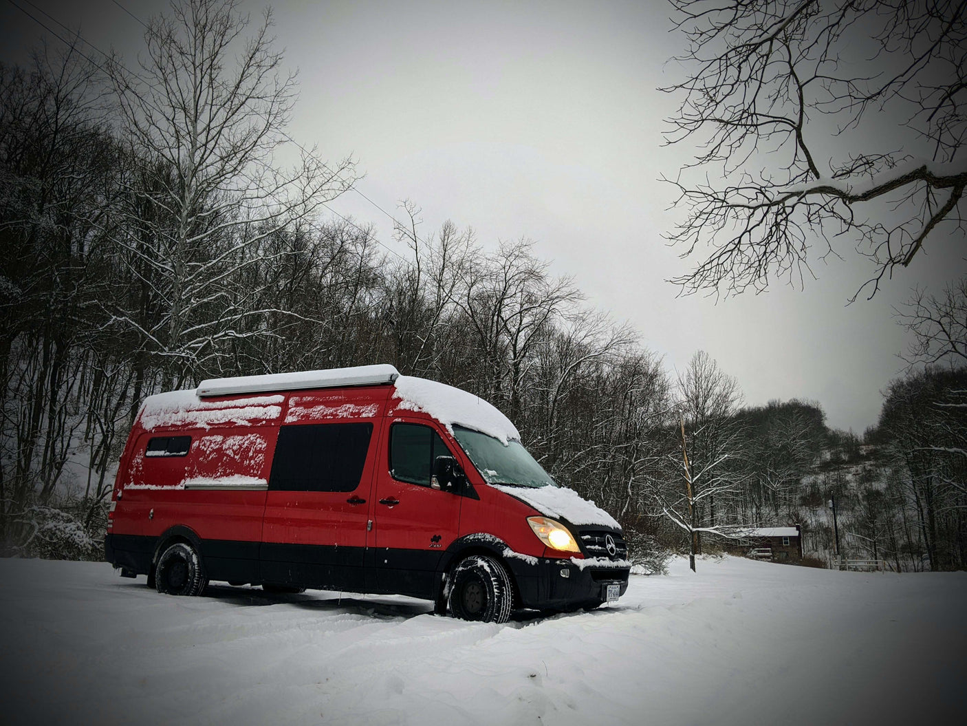 Red RV rental van, a Mercedes Sprinter, covered in snow amidst a winter landscape, ready for adventure.