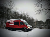 Red RV rental van, a Mercedes Sprinter, covered in snow amidst a winter landscape, ready for adventure.