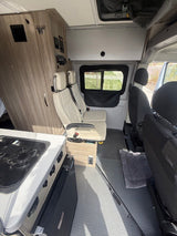 Spacious rv rental interior: A modern camper van features a kitchenette, two light quilted passenger seats, and overhead storage.