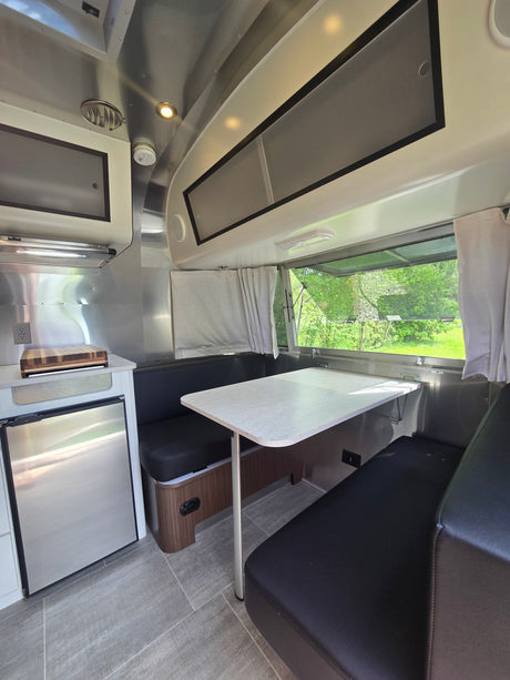 Compact Airstream RV rental interior with dinette, kitchenette, and scenic window view for your road trip adventure.