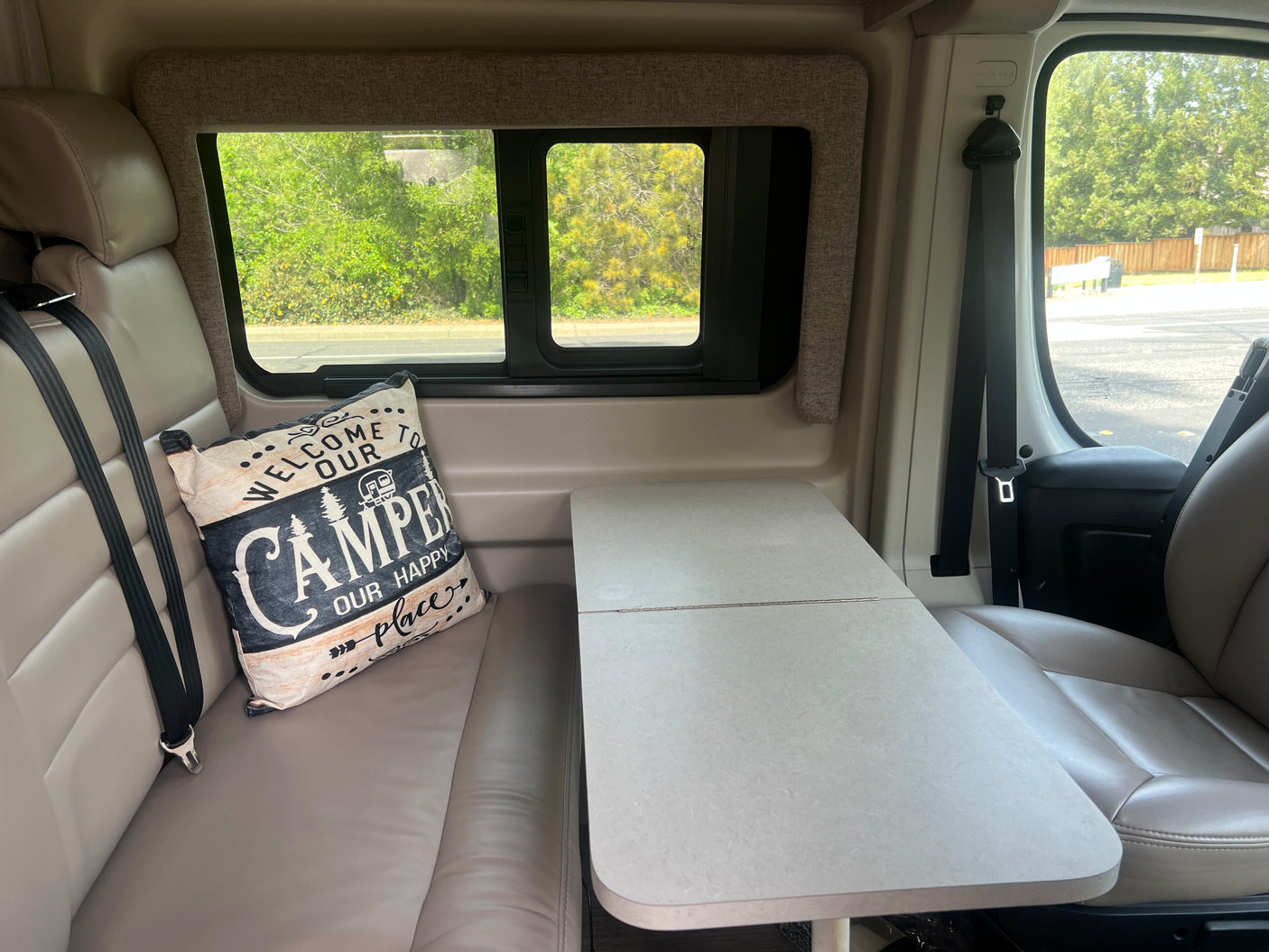 Inside an RV rental: a cozy dinette with bench seating, a "CAMPER" pillow, and a versatile table.
