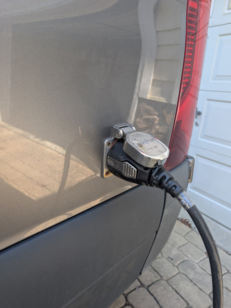 Powering an RV rental: A SmartPlug shore power cord connected to the side of a grey RV, parked on pavers near a garage.