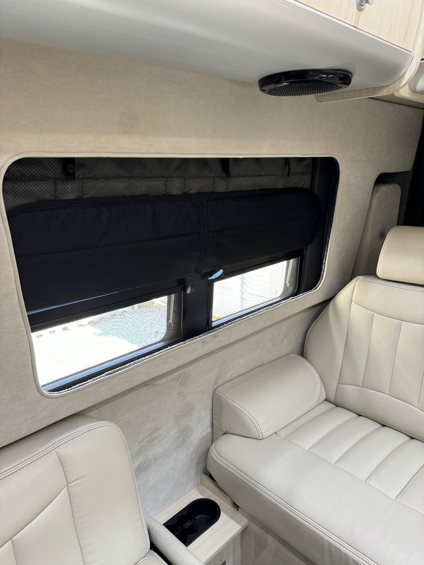 Inside an RV rental: plush beige seats, a window with a black blind, and built-in cup holders for comfortable travel.