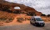 Grey RV rental parked near a majestic natural arch. This camper van is ideal for desert travel and exploring rock formations.