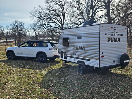 White Jeep Grand Cherokee L towing a Forest River Puma travel trailer. Ideal for your next RV rental adventure.