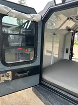 Inside an RV rental: View from the open side door of a camper, revealing a comfortable sleeping area and interior.