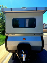 Explore the outdoors! This compact RV rental, a towable camper, features a raised roof and rear window. Ideal for adventure.