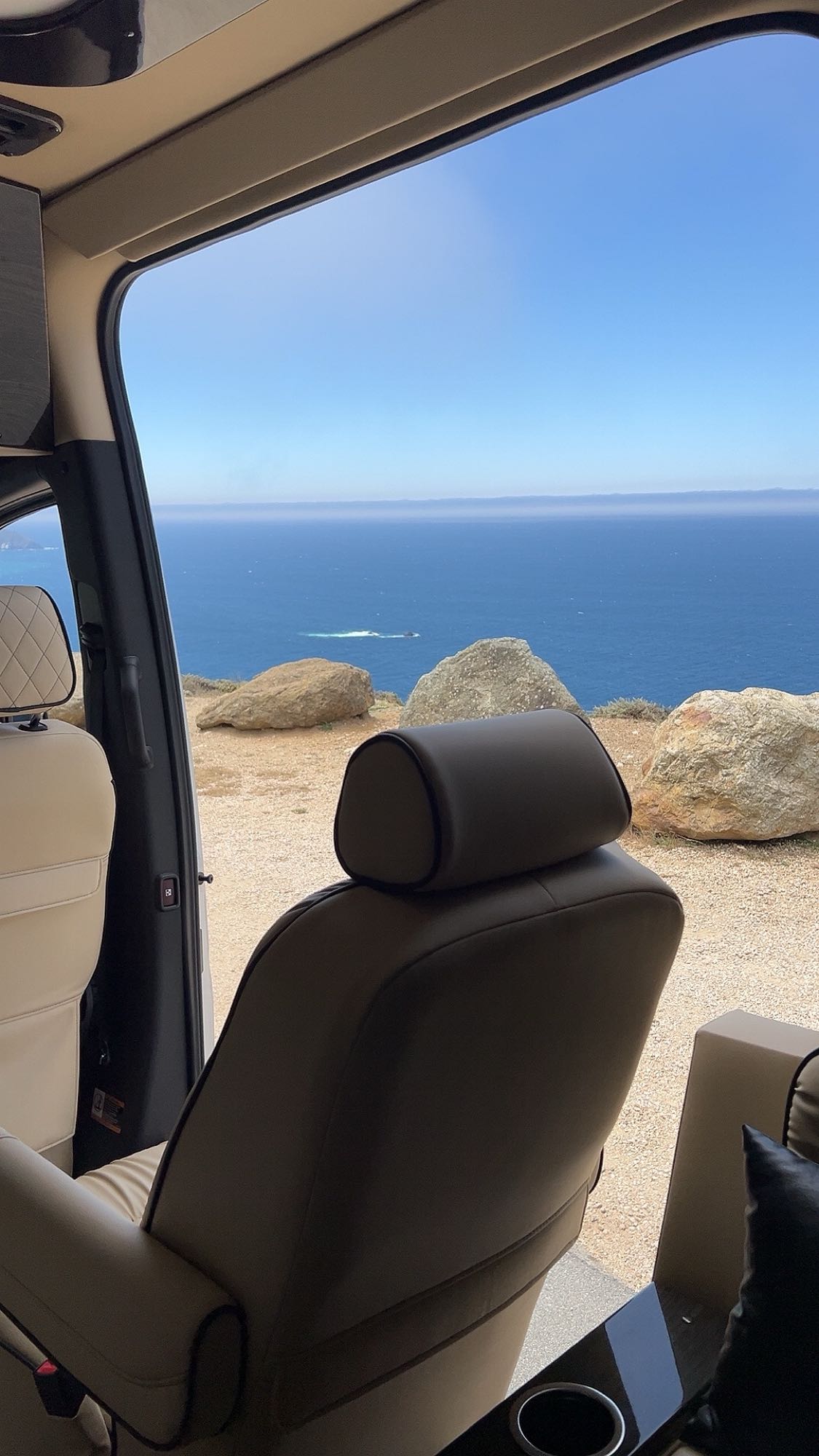 Open door of an RV rental reveals stunning ocean views from a clifftop. Enjoy the comfort of this luxury camper van.