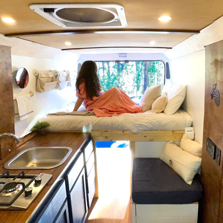 Step into this **RV rental**: a woman relaxes on an elevated bed, overlooking a compact kitchen and seating area. Enjoy the view!
