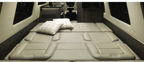 Spacious RV rental interior features a large, comfortable bed with pillows and a compact kitchenette.