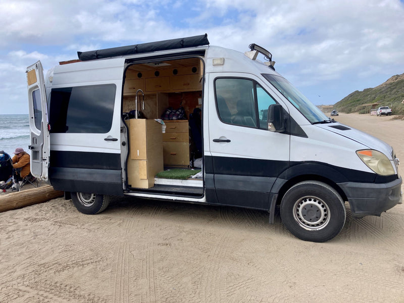Converted camper van, resembling an RV rental, parked on sandy beach. Open door reveals a custom interior, ready for travel adventures by the ocean. — photo 1