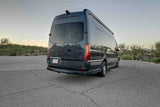 Dark grey Mercedes Sprinter RV rental, seen from the rear-side, parked on asphalt with a desert landscape. Ideal for travel.