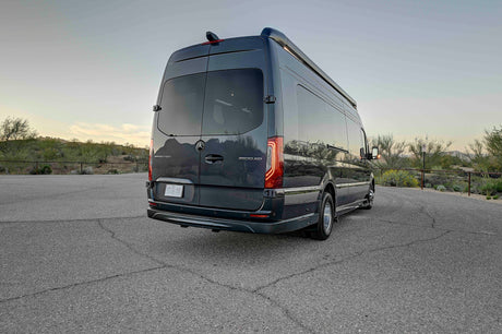 Dark grey Mercedes Sprinter RV rental, seen from the rear-side, parked on asphalt with a desert landscape. Ideal for travel.