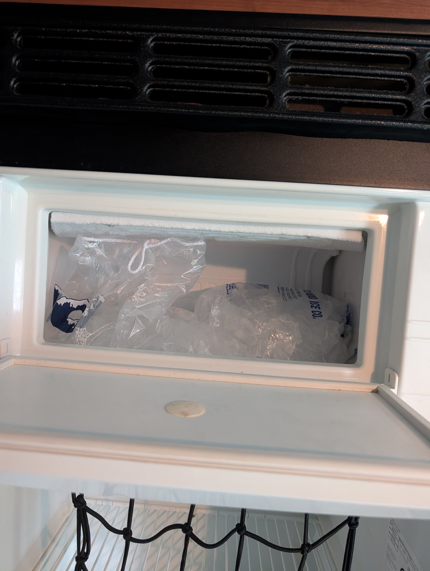 An RV rental's compact freezer, stocked with bags of ice and a frosted top shelf, keeps items cold for your travels.