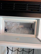 An RV rental's compact freezer, stocked with bags of ice and a frosted top shelf, keeps items cold for your travels.