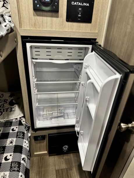 RV rental interior features a clean, empty fridge, bunk bed, and Catalina control panel. Perfect for camping trips.