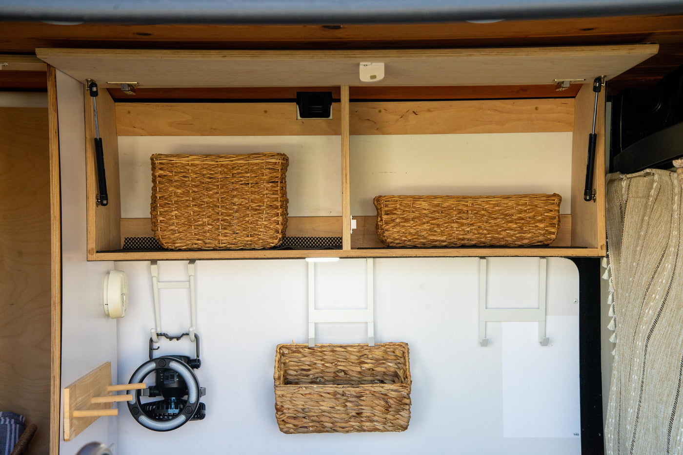 Efficient RV rental storage: overhead cabinets with wicker baskets, a fan, and organizational hooks in a cozy camper interior. — photo 19