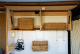 Efficient RV rental storage: overhead cabinets with wicker baskets, a fan, and organizational hooks in a cozy camper interior.