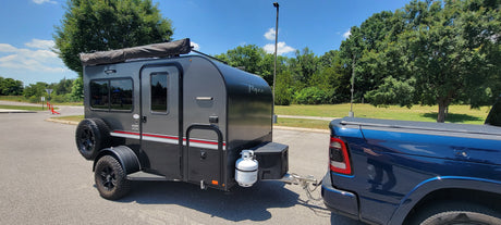 Dark grey teardrop rv rental trailer hitched to a blue pickup, ready for adventures on a sunny day.