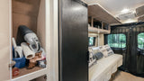 RV rental interior: organized compact living space with a full-size fridge, overhead storage, and a well-stocked utility cabinet.