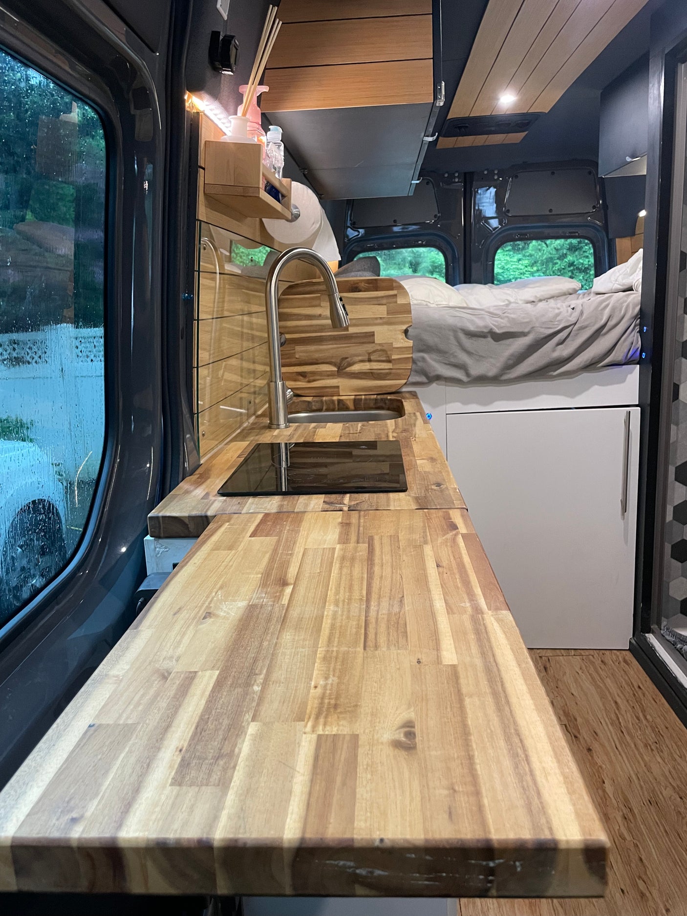 Cozy RV rental interior: kitchen with wooden counter, sink, cooktop, and built-in bed. Ideal for road trips!