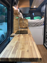 Cozy RV rental interior: kitchen with wooden counter, sink, cooktop, and built-in bed. Ideal for road trips!