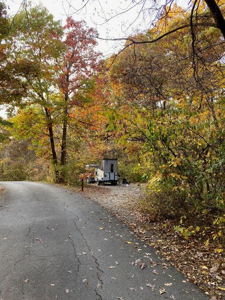 Autumn camping: A compact RV rental is nestled among colorful fall trees at a cozy campsite.