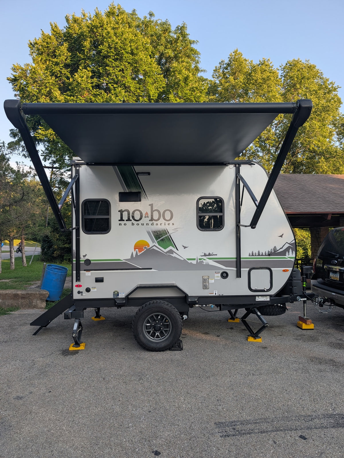 This "No Boundaries" RV rental, a white travel trailer with its awning extended, is parked on asphalt with stabilizing jacks.
