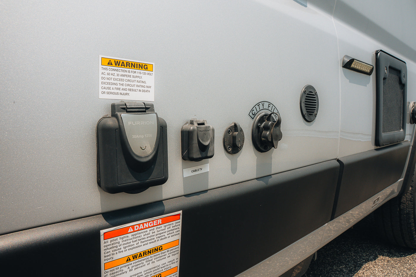 RV rental showing side utility panel with 30A power, cable TV, city water hookups, and safety warnings.