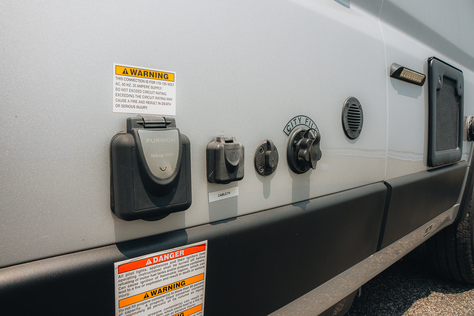 RV rental showing side utility panel with 30A power, cable TV, city water hookups, and safety warnings.
