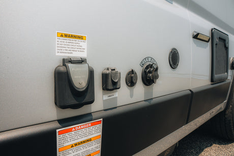 RV rental showing side utility panel with 30A power, cable TV, city water hookups, and safety warnings.