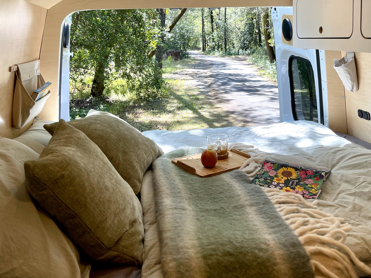 Cozy RV rental interior with a bed, pillows, breakfast tray, and beautiful nature view out the open doors.