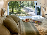 Cozy RV rental interior with a bed, pillows, breakfast tray, and beautiful nature view out the open doors.