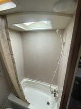 Compact RV rental shower and bathtub with a striped curtain and ceiling skylight, ready for your travel needs.
