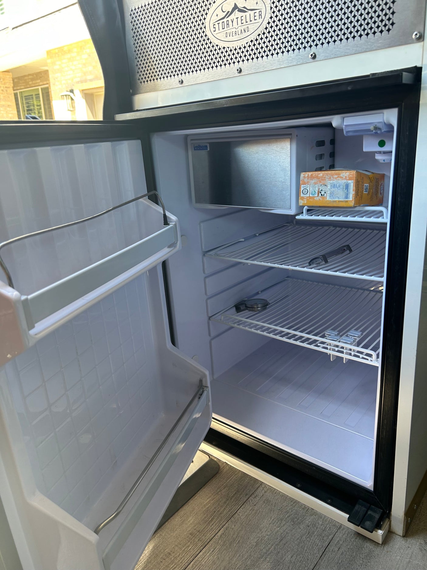 RV rental kitchen: Interior of a clean, compact refrigerator with open door, empty shelves, and a small freezer.