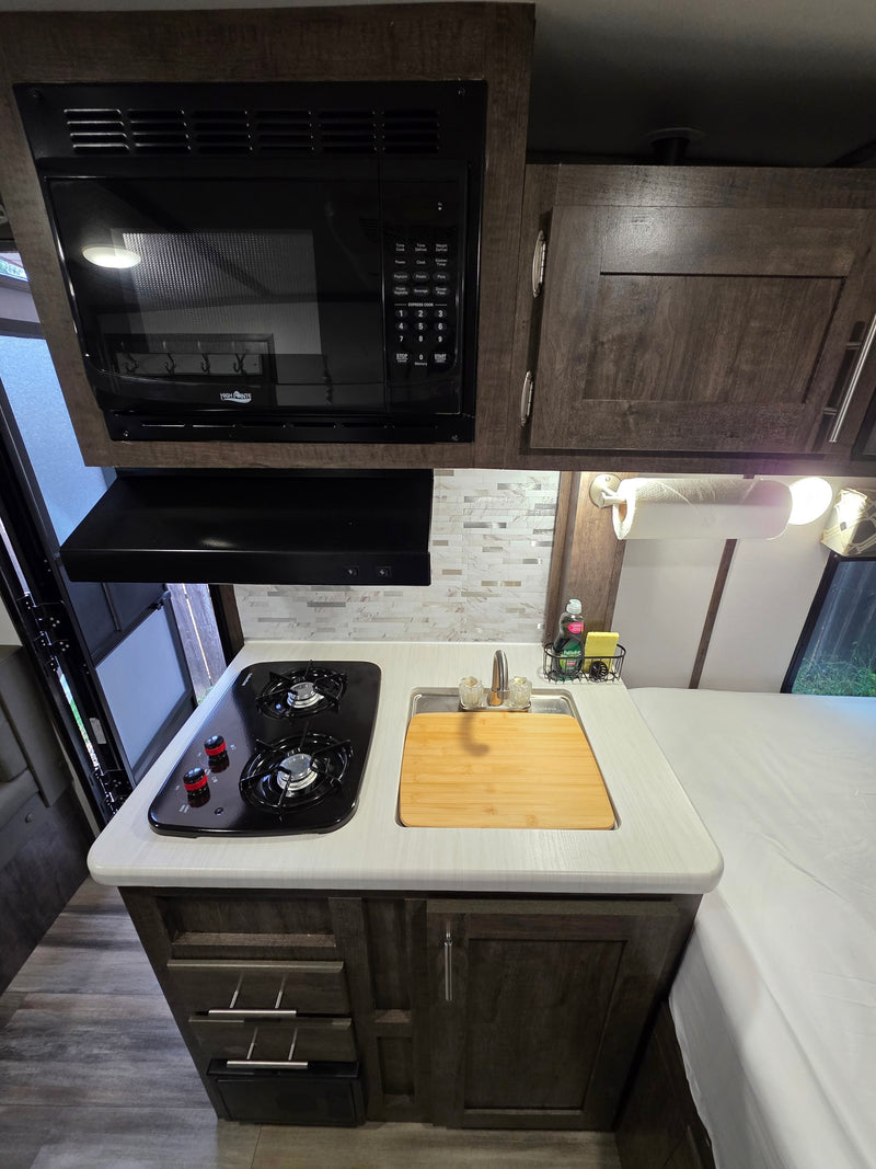 Modern RV rental kitchenette: High Pointe microwave, 2-burner stove, sink, and storage. Ideal for travel. — photo 7