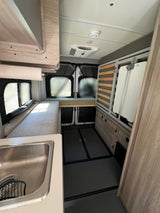Explore this functional RV rental interior featuring a kitchen sink, convertible bed, and ceiling AC unit.