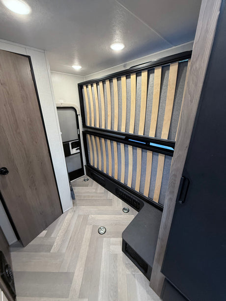 Inside an RV rental: two stacked bunk beds with slatted bases, light herringbone floor, and an exit door in the back.